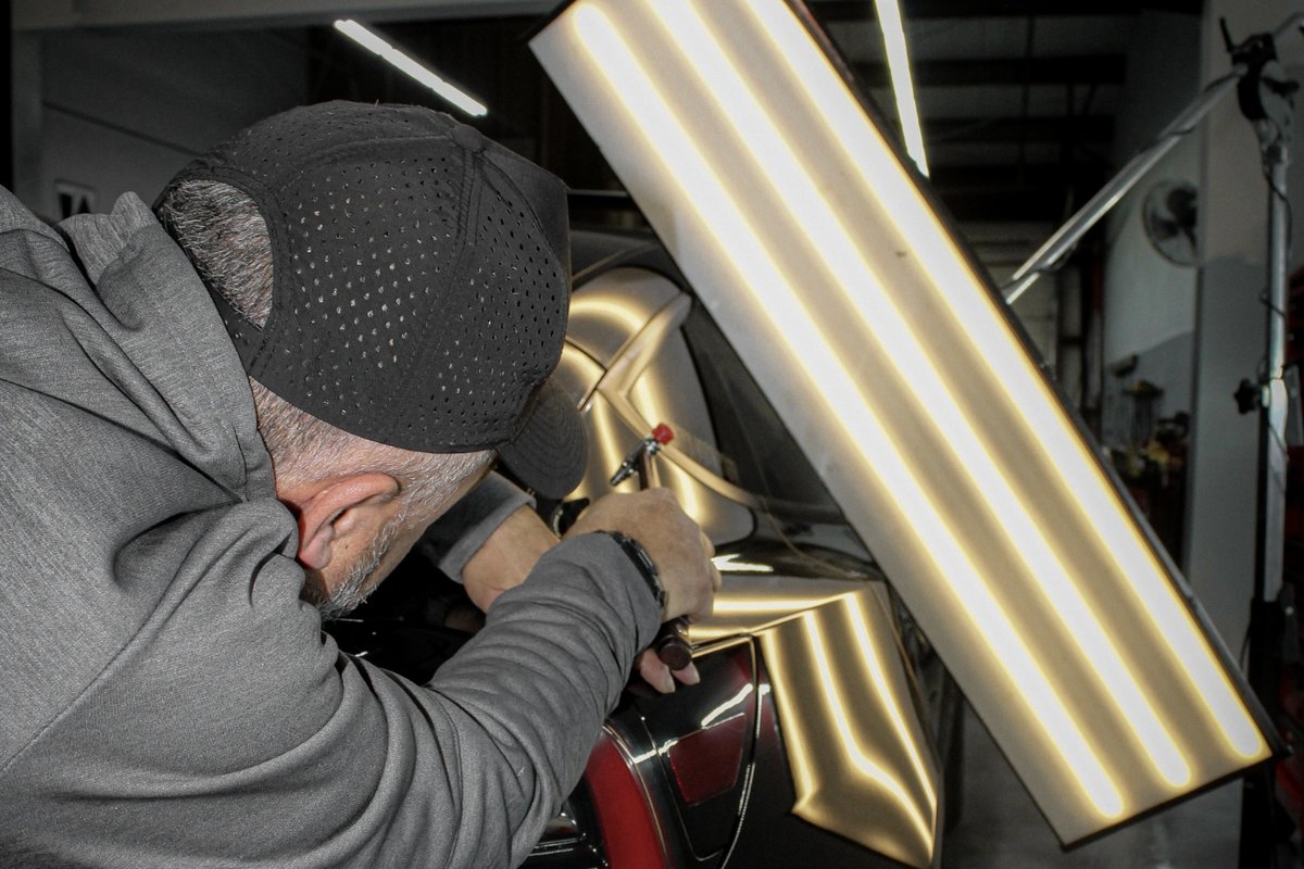 Technician reading panel reflections under a light board during paintless dent repair