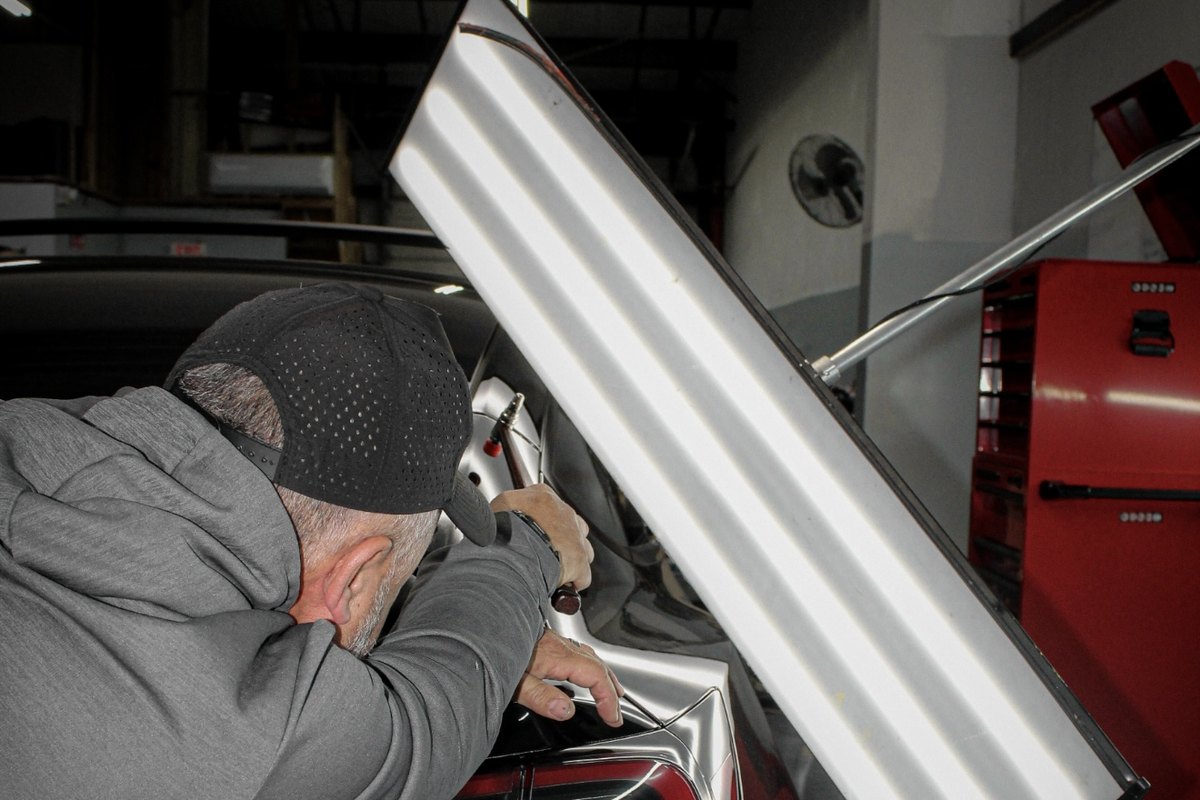 Paintless dent repair on a black vehicle panel with light-line reflection board