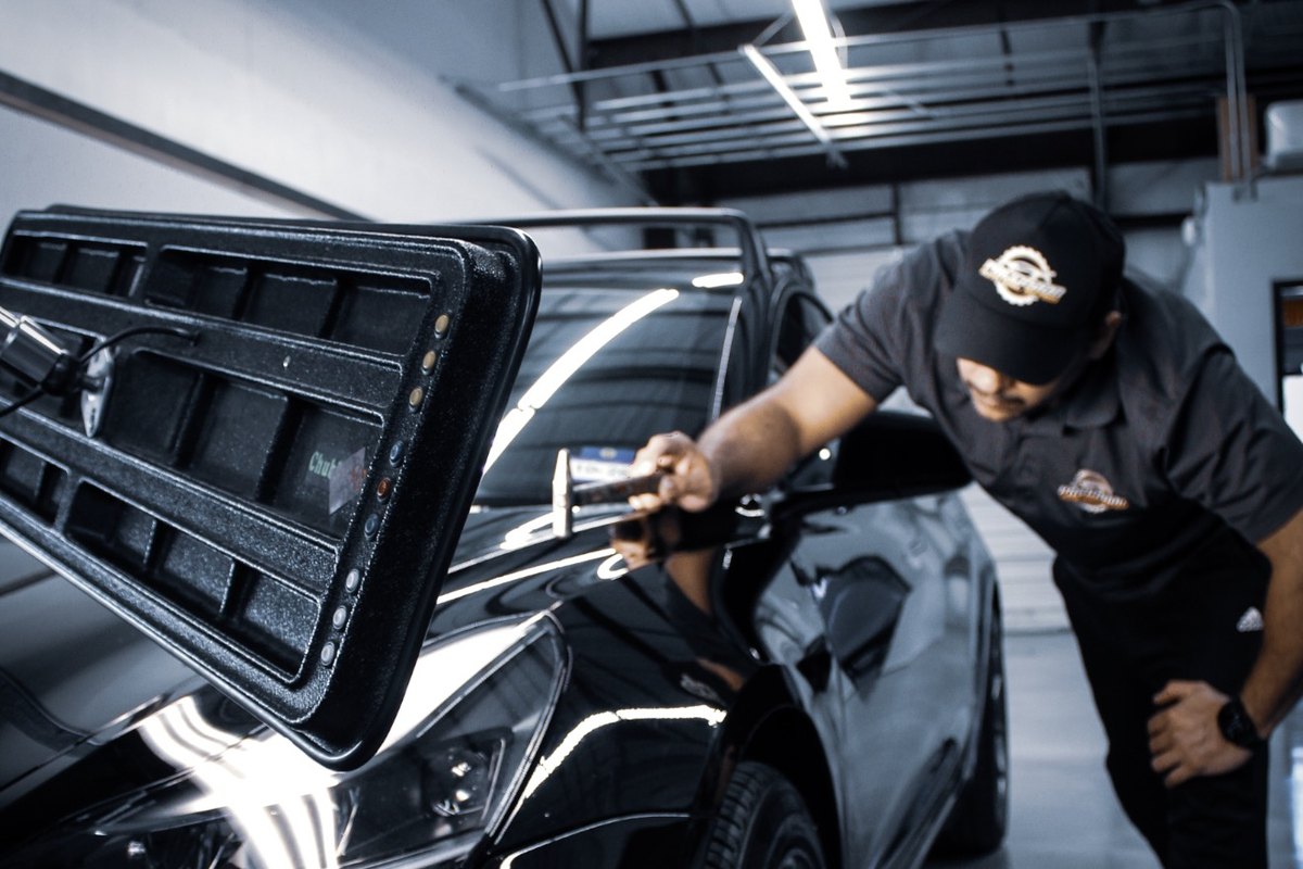 Master technician working a dent on a black car under a reflection board